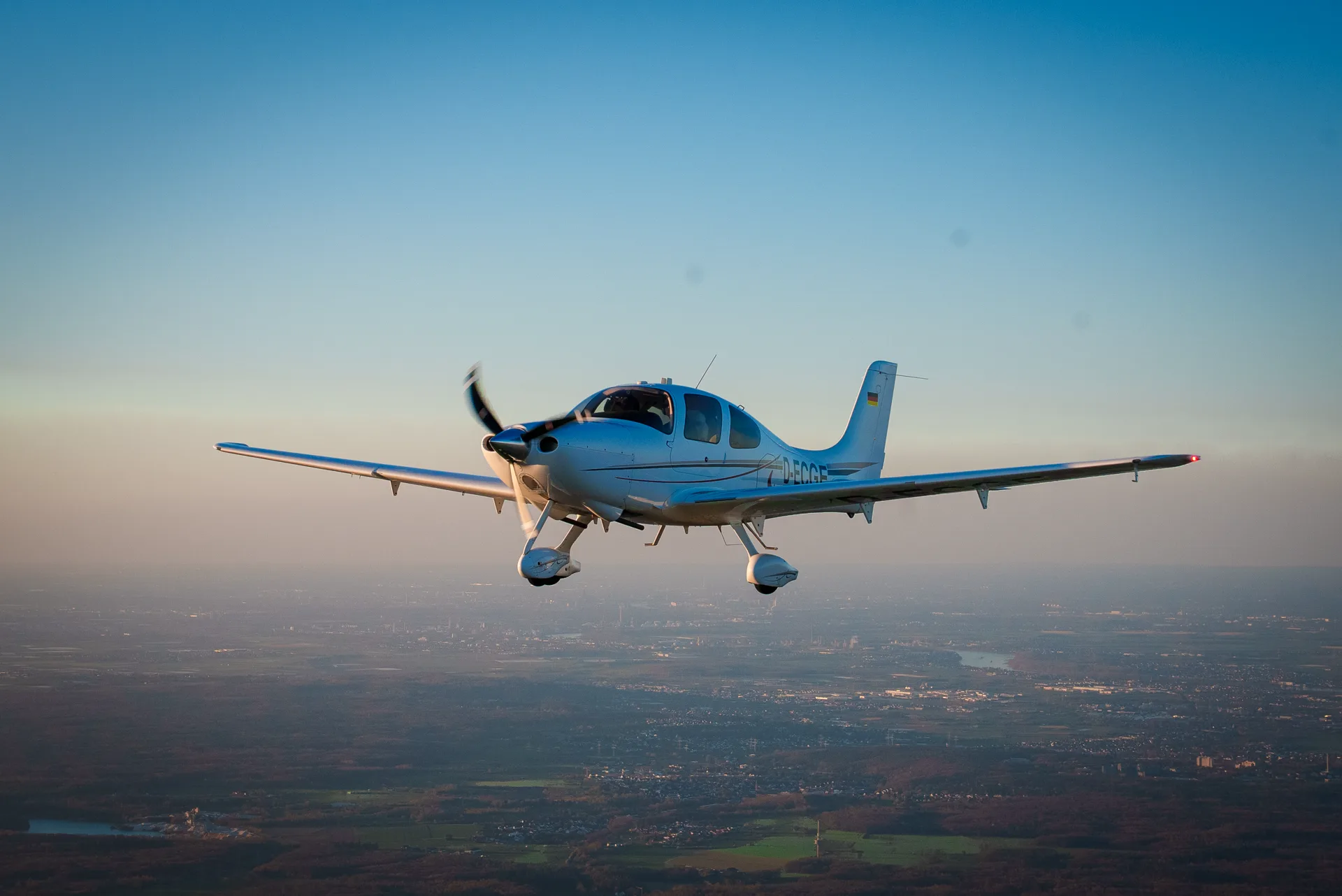 Kleinflugzeug der AAT Flugschule im Sinkflug über Feldern im goldenen Abendlicht